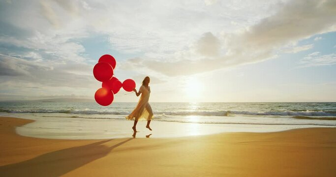 Beautiful happy young woman playing with red balloons on the beach
