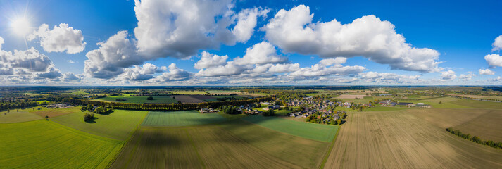 Sunny panorama of rural idyll with fields, long lime tree avenue and village in the countryside....