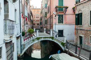 Bridge across narrow water canal in Venice between old buildings with balconies and brick walls. Italy.