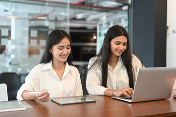 A diverse team of two coworkers working over a laptop at modern office.