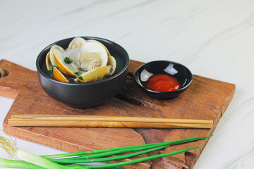 Kerang Kapah Rebus or boiled hard clam served on ceramic bowl on white marble background. Copy space.