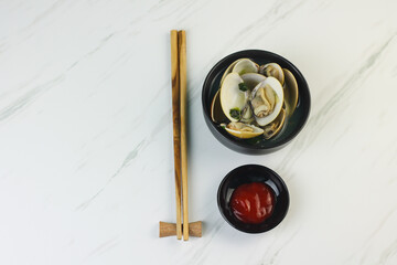Kerang Kapah Rebus or boiled hard clam served on ceramic bowl on white marble background. Copy space.