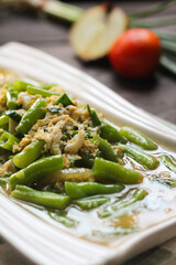 Buncis Telur, Green Bean and Egg Stir Fry, a simple delicious green bean cooked with scrambled egg and spices. White ceramic plate on wooden background