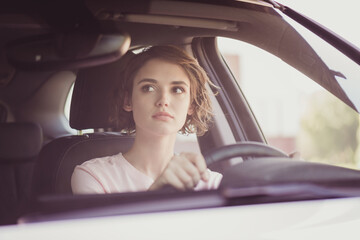 Obraz na płótnie Canvas Photo of charming pretty lady calm concentrated face hands hold steering wheel drive car carefully watch rearview mirror wait another driver make turn wear white shirt indoors