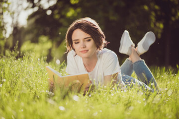 Full body size photo of charming lovely cute lady smiling reading nice romantic novel textbook lying grass in harmony world nature resting wear jeans sneakers white shirt outside
