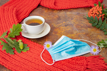 A medical mask, a red scarf, a cup of tea, a mountain ash on the table. Flatley. Concept, autumn, quarantine, covid