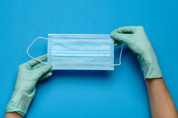 Human hand in protective gloves holding face protective mask isolated on blue background