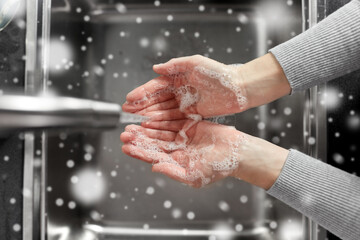 hygiene, health care and safety concept - close up of woman washing hands with soap and water in kitchen at home in winter over snow
