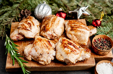 Christmas chicken thighs grilled without skin on a background of a stone with fir trees and fir toys, gifts 