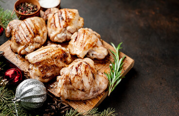 Christmas chicken thighs grilled without skin on a background of a stone with fir trees and fir toys, gifts with copy space for your text