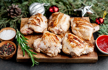Christmas chicken thighs grilled without skin on a background of a stone with fir trees and fir toys, gifts