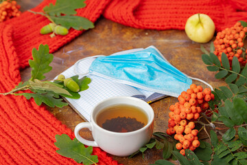 A medical mask, a red scarf, a cup of tea, a mountain ash on the table. Flatley. Concept, autumn, quarantine, covid