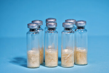 Glass vials of vaccine on a blue background, lined up in a row. The concept of vaccination of the population against influenza and coronavirus. Selective focus, close-up, copy space.