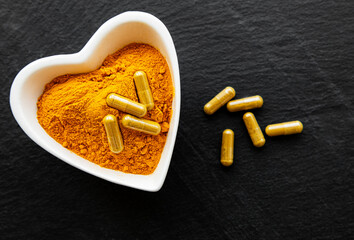 Turmeric powder and turmeric pills on a black concrete background