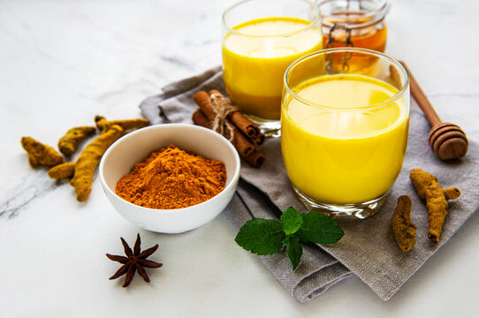 Yellow turmeric latte drink. Golden milk with cinnamon, turmeric, ginger  and honey over white marble background.