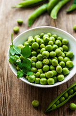 Green peas in white bowl with fresh pods on the wooden table, top view or flat lay