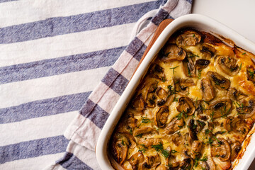 Mushroom julienne in a baking dish stands on a Board and on a kitchen towel on a white background
