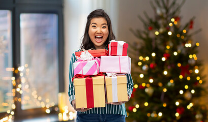 Fototapeta na wymiar winter holidays and people concept - happy asian young woman with gift box over christmas tree on background