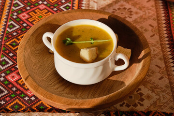 yellow soup with breadcrumbs in a white cup on a wooden plate