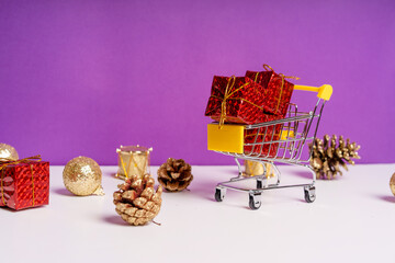 The concept of new year's holiday sales. Mini cart with gifts on a purple background with scattered Christmas decorations around