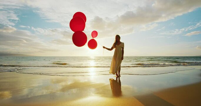 Beautiful happy young woman holding red balloons on the beach at sunset, happiness and wellness concept