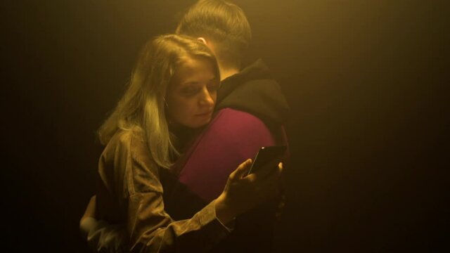 Beautiful couple in love caucasian guy and girl stand embracing and look at smartphones on a black background. Hostages of new technologies and smartphones, slow motion