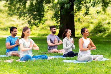 Fototapeta premium fitness, sport, yoga and healthy lifestyle concept - group of happy people meditating in lotus pose at summer park