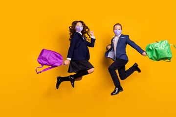 Full body size photo of two pupils jumping having fun wear uniform medical mask isolated vibrant yellow color background