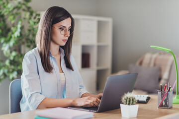 Photo of serious young lady sit chair hands typing keyboard laptop wear spectacles shirt in home office indoors