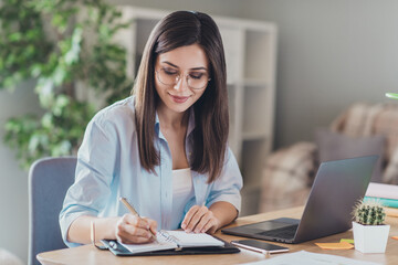 Photo of pretty young girl sit desktop pc hold pen write notepad wear glasses shirt in home office...