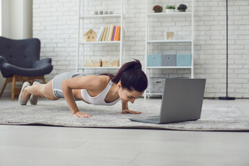 Online home sports. Young fit woman exercising to video tutorial indoors, doing plank or push up exercise