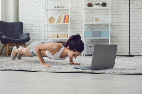 Online home sports. Young fit woman exercising to video tutorial indoors, doing plank or push up exercise