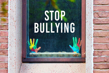 Stop bullying written on the window of a building with mockup child hands. Bullying problem at school