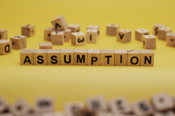ASSUMPTION Word Written In Wooden Cube With Yellow Background