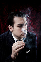 Studio photo of a well dressed man with dark hair smoking a cigarette.