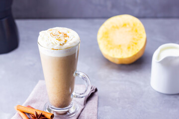 Pumpkin spice latte on a gray background. Pumpkin latte with whipped cream, coffee maker and milk jug. Hot autumn drink on cement background