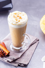 Pumpkin spice latte on a gray background. Pumpkin latte with whipped cream, coffee maker and milk jug. Hot autumn drink on cement background