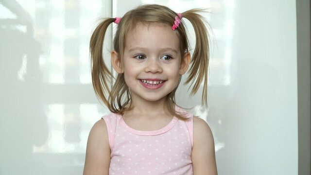 Close up of little funny girl laughs, smiles and catches multicolored confetti. Kid gets scared and flinches by loud sound of petard. Happy child celebrates birthday.