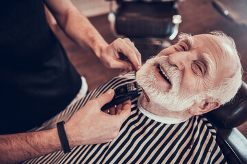 Old grandfather smiles as he gets his hair cut. 