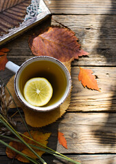 Hot cup of tea on a wooden background. White cup with tea and lemon on an autumn day. Autumn colorful leaves. Cozy concept. Top horizontal view.