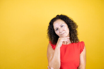 Middle age woman wearing casual shirt standing over isolated yellow background thinking looking tired and bored with crossed arms