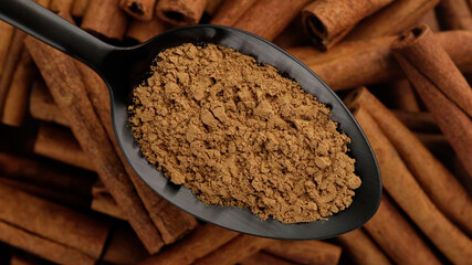 cinnamon powder in spoon and cinnamon stick on background