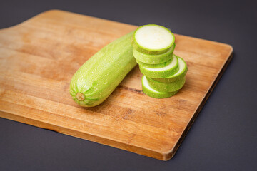 Slices of courgettes on wooden chopping board. Fresh green zucchini whole and cut into slices on cutting board