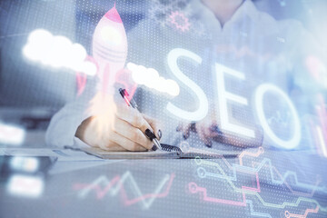 Multi exposure of woman's hands making notes with SEO icon. Concept of Search engine optimization