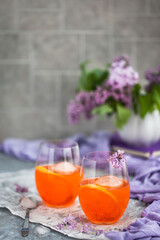 Orange Aperol Spritz cocktail served in a wine glasses, decorated with slice of orange and lilac
