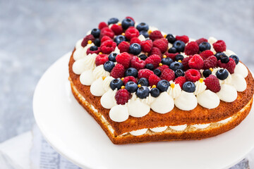 Delicious homemade heart shaped vanilla cake decorated with cream and fresh berries