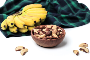 Brazil Nuts in a wooden bowl and bunch of baby bananas on green checkered tablecloth isolated on white background. Clipping path included