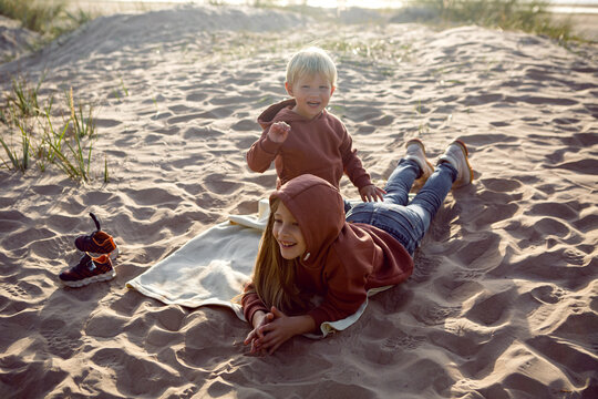 brother and sister in a hoodie sit on the sand