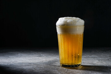full faceted glass with beer and foam on gray background
