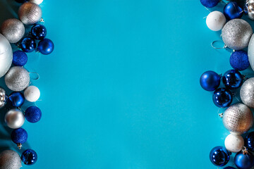 Shiny Christmas balls in blue, white and silver are arranged in a row on a turquoise background with a space for text.